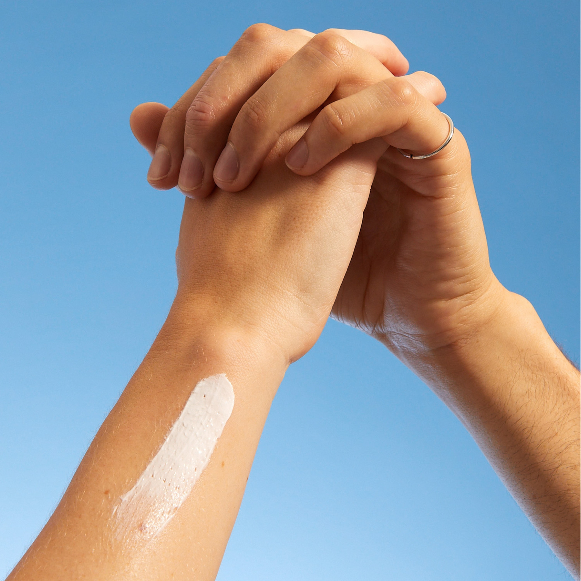 Hände mit Sonnencreme auf dem Arm vor blauem Himmel