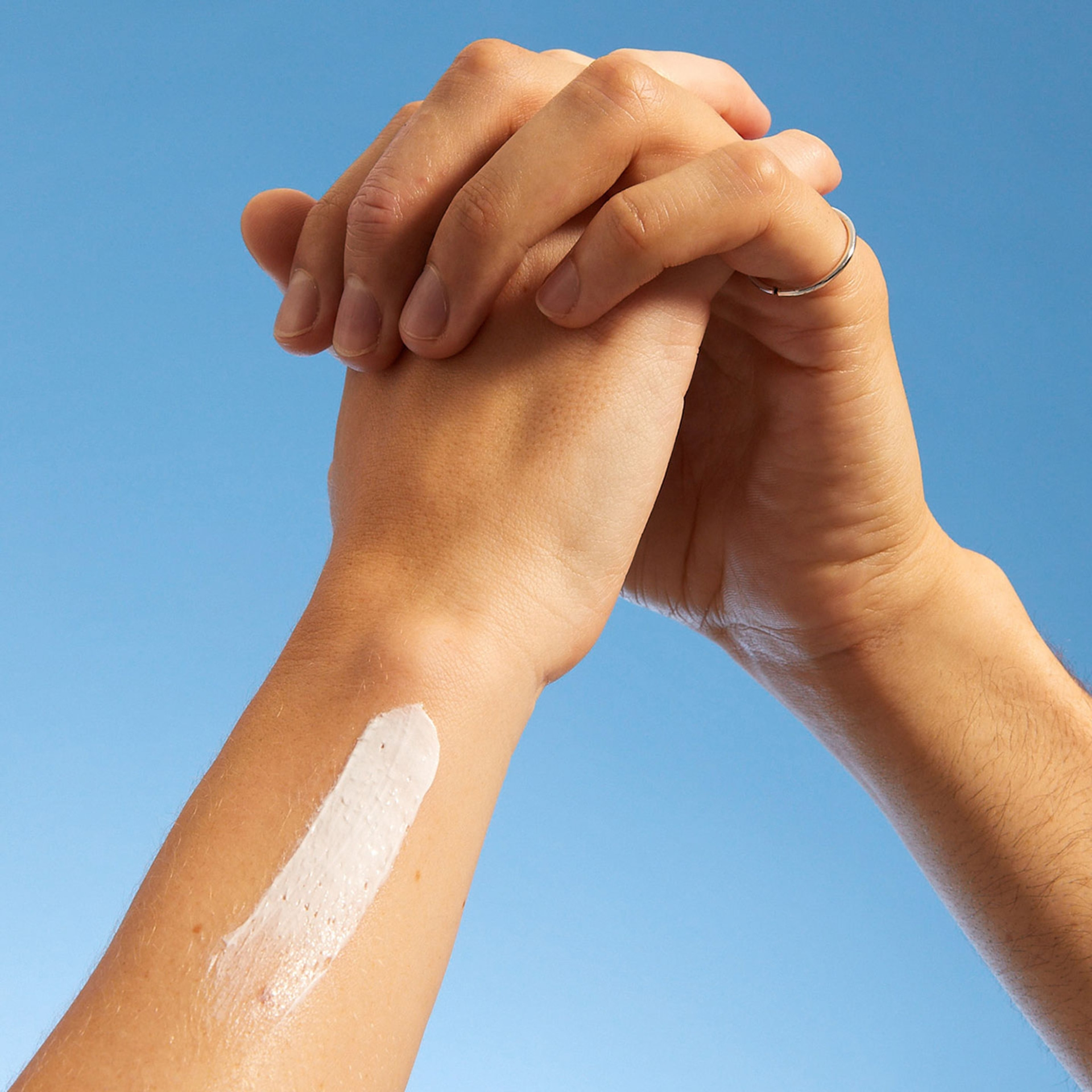 Hände mit Sonnencreme auf dem Arm vor blauem Himmel